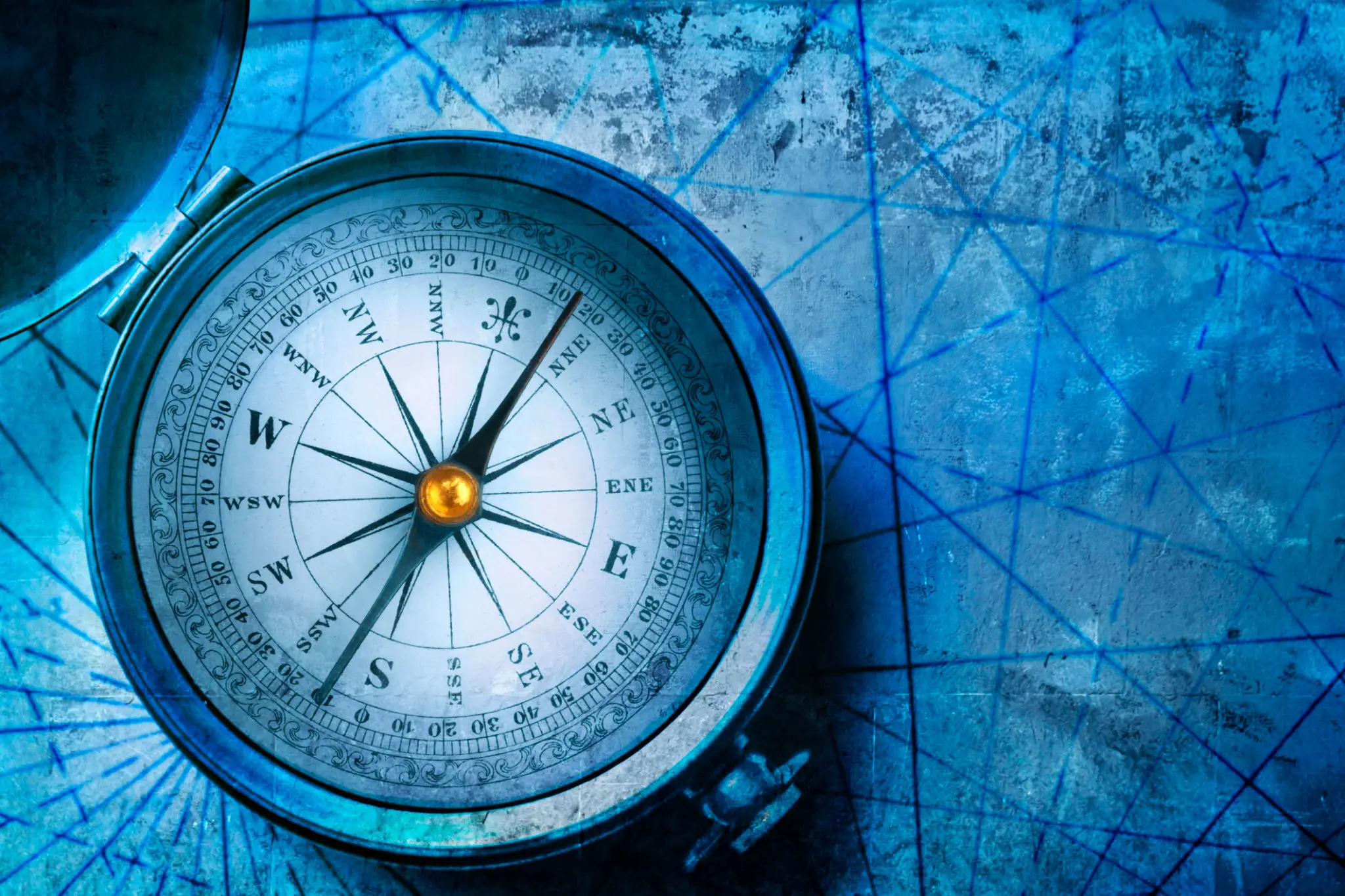 An old-fashioned silver compass rests on a blue nautical map, with the compass needle pointing north.